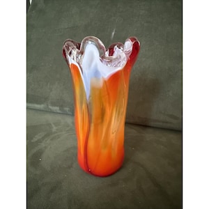May include: A colourful, hand-blown glass vase with a flared, ruffled rim. The vase features a blend of orange, red, white, and yellow hues, creating a dynamic design. The vase is a decorative item, suitable for displaying flowers or as a standalone art piece.
