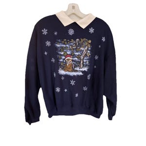 May include: Navy blue sweatshirt with a white collar and a winter scene graphic. The graphic features a bear wearing a Santa hat and scarf, surrounded by snowflakes. A cozy, festive garment for the holiday season.