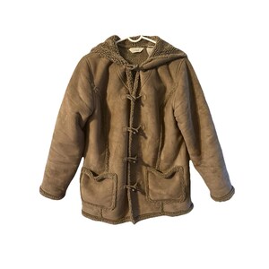 May include: A tan suede-like jacket with a hood and toggle closures. The jacket has two front pockets and a fuzzy lining around the hood and cuffs. The jacket is hanging on a white hanger.