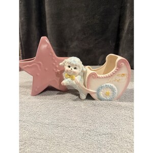 Könnte beinhalten: Vintage Keramik-Kinderzimmer-Set mit einem sternförmigen rosa Pflanzgefäß und einem Kinderwagen-Pflanzgefäß mit einer Lammfigur. Der Wagen ist weiß und hellblau mit rosa Akzenten. Das Lamm hat eine gelbe Fliege.