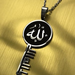 Op de afbeelding: Een zilverkleurige hangerketting met een sleutelontwerp. De sleutel heeft een cirkelvormige zwarte hanger met witte Arabische kalligrafie. De ketting is ook zilverkleurig en de achtergrond is goudkleurig geborsteld.