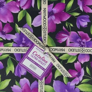 May include: A fabric bundle featuring a floral pattern with purple and violet flowers and green leaves on a black background. The bundle is tied with a ribbon that reads "MAYWOOD STUDIO". A tag reads "Catalina Ultra Violet" and "10 inches".
