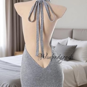 May include: A gray, backless knitted dress with a high turtleneck and long ties. The dress is displayed on a mannequin, showcasing its open back design. The hemline falls just above the knees.