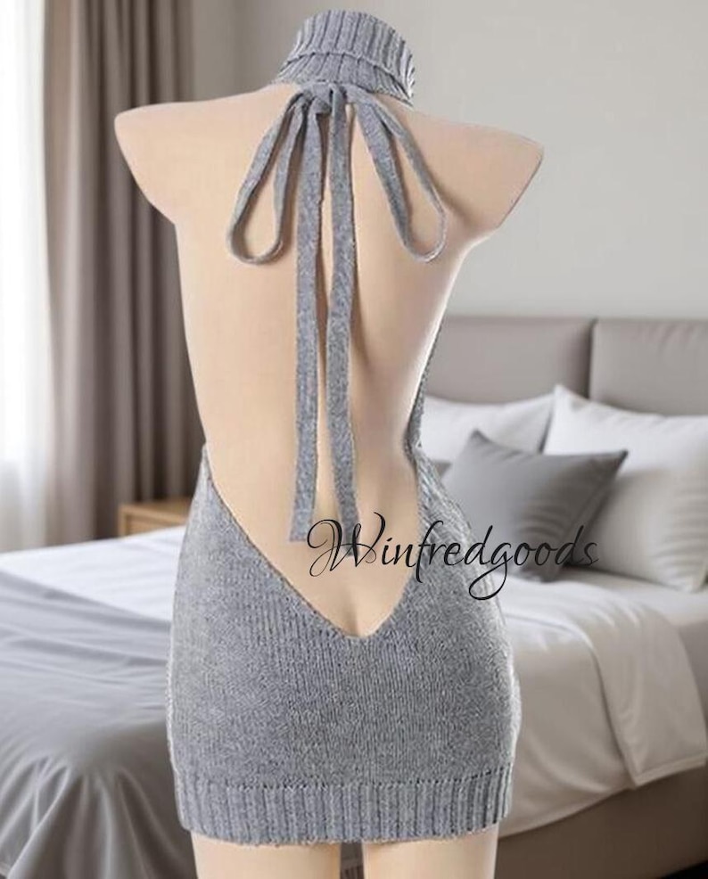 May include: A gray, backless knitted dress with a high turtleneck and long ties. The dress is displayed on a mannequin, showcasing its open back design. The hemline falls just above the knees.