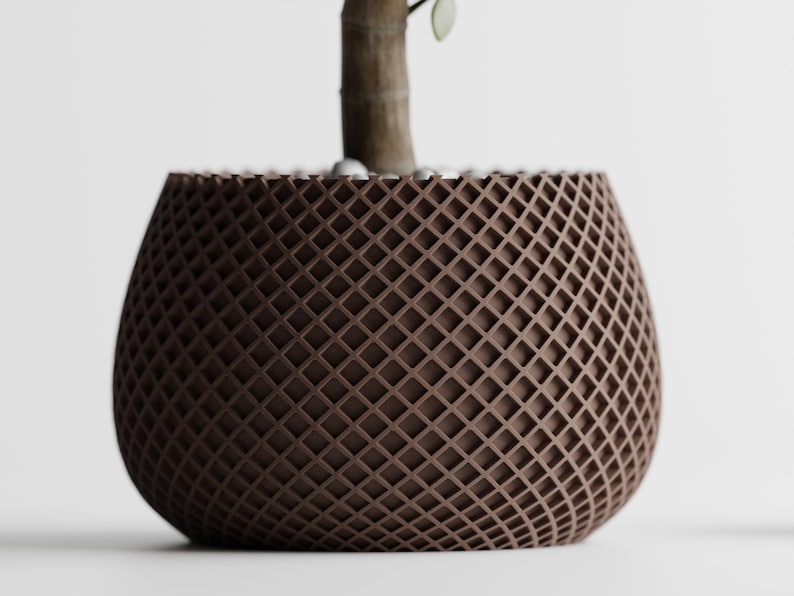 May include: A brown, lattice-patterned plant pot with a rounded shape. The pot has a textured surface and is designed to hold a plant. The top of the pot is filled with small white stones, and a plant stem is visible.