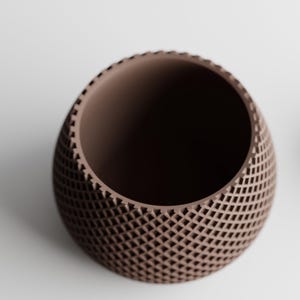May include: A brown, egg-shaped decorative bowl with a lattice pattern. The bowl has a smooth interior and a textured exterior. The design features a series of small, evenly spaced openings, creating a geometric pattern. The bowl is likely made of ceramic or a similar material.