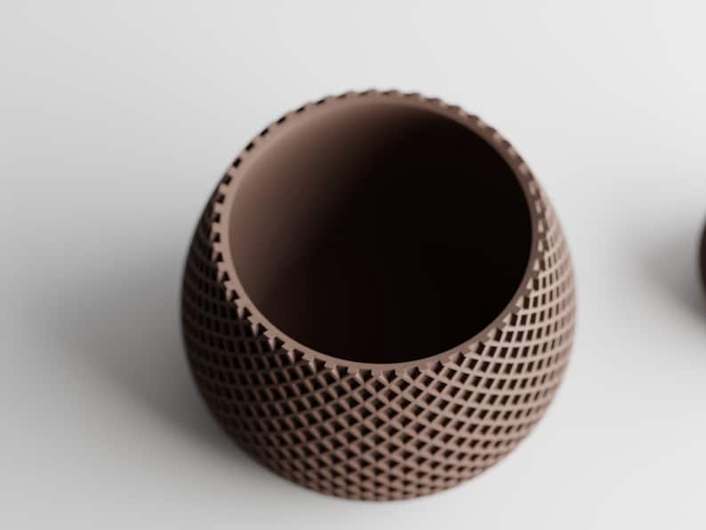May include: A brown, egg-shaped decorative bowl with a lattice pattern. The bowl has a smooth interior and a textured exterior. The design features a series of small, evenly spaced openings, creating a geometric pattern. The bowl is likely made of ceramic or a similar material.