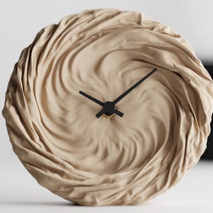Può includere: Un orologio da parete rotondo beige con un quadrante unico e strutturato. Il quadrante presenta un design a spirale, simile a un tessuto. Lancette nere e un centro color oro completano il design. Un moderno oggetto di arredamento per la casa.