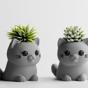 May include: Two gray cat-shaped planters, each holding a small succulent. The planters have large black eyes, whiskers, and a small nose. One cat is sitting, the other is in a seated position. A charming addition to any home decor.