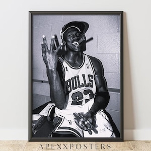 May include: Black and white framed print featuring a basketball player in a Chicago Bulls jersey, number 23. The player is holding up three fingers and smoking a cigar. The image is a portrait.