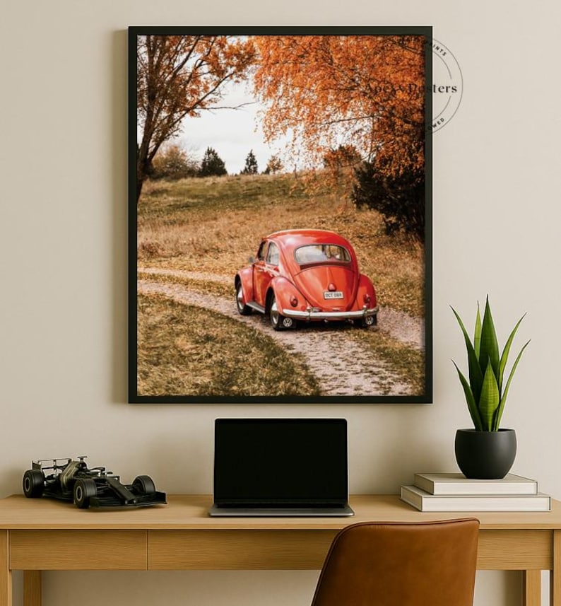 May include: A framed wall art print featuring a red vintage Volkswagen Beetle parked on a dirt path surrounded by autumn trees with orange foliage. The scene captures the rear view of the car in a rural landscape setting with a clear sky above.