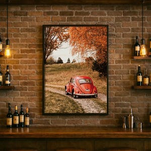 May include: A framed wall art print featuring a red vintage car parked on a dirt path in a field with autumn trees. The scene is displayed on a rustic brick wall above a wooden bar counter with several glass bottles and hanging pendant lights.