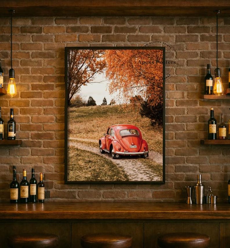 May include: A framed wall art print featuring a red vintage car parked on a dirt path in a field with autumn trees. The scene is displayed on a rustic brick wall above a wooden bar counter with several glass bottles and hanging pendant lights.