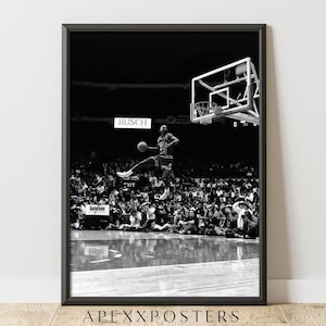 Op de afbeelding: Zwart-wit ingelijste print van een basketballer in de lucht, op het punt om de bal te dunken. De speler draagt een shirt met nummer 23. De achtergrond toont een menigte en een basketbalring.