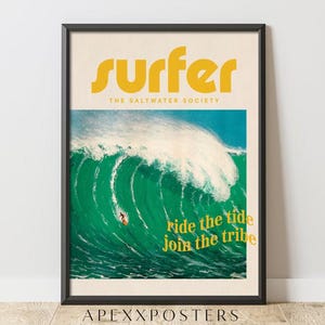 Op de afbeelding: Een ingelijste poster met een grote groene oceaangolf met een surfer op een plank. De tekst luidt SURFER THE SALTWATER SOCIETY bovenaan en ride the tide join the tribe in het geel rechtsonder. De achtergrond heeft een crèmekleur.