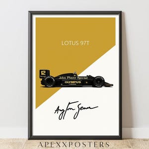 May include: Framed poster of a black Lotus 97T race car with gold detailing, the text "LOTUS 97T", and Ayrton Senna's signature. The background is split diagonally, with a gold upper section and a white lower section.