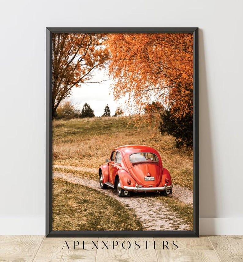 May include: A framed wall art print featuring a bright red vintage Volkswagen Beetle parked on a dirt path. The scene is set in an autumn landscape with golden-orange trees and dry grass. The text APEXXPOSTERS is printed at the bottom of the frame.