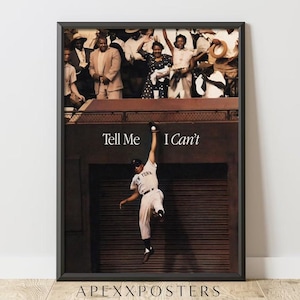 Op de afbeelding: Een ingelijste poster met een sepia-kleurige foto van een honkbalspeler in een wit uniform die tegen een donkere muur opspringt om een bal te vangen. Boven de speler staat de tekst Tell Me I Can't. Op de achtergrond is een menigte toeschouwers zichtbaar.