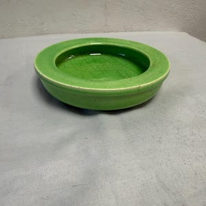 May include: A round, green ceramic bowl with a wide rim. The bowl has a glossy finish and a crackle pattern on the inside. The bowl is sitting on a light gray surface.