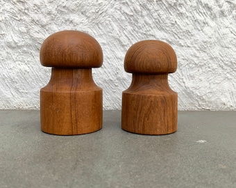 May include: Two wooden salt and pepper shakers shaped like mushrooms. The shakers are made of dark brown wood and have a smooth, polished finish.