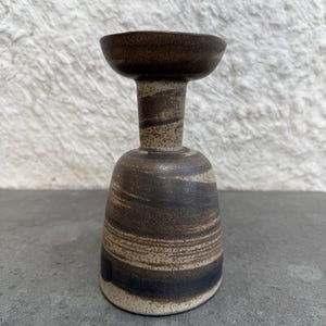 May include: A ceramic goblet with a wide, flared rim and a narrow neck, featuring a marbled pattern of dark brown, black, and cream tones. The surface has a speckled, textured appearance with horizontal bands of color wrapping around the body.
