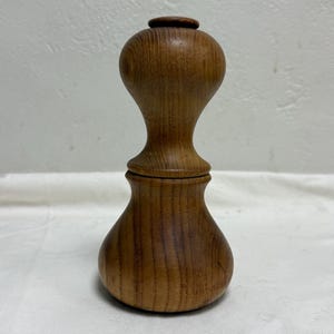 May include: A handcrafted wooden container with a bulbous base and a narrower, elongated top. The container is made of light brown wood, showcasing the natural grain. The design features a lid and a rounded top, suggesting a decorative or storage item.