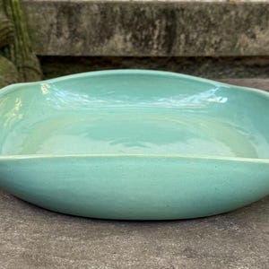 Könnte beinhalten: Eine helltürkisfarbene Keramik-Servierschüssel mit rechteckiger Form und sanft geschwungenen Kanten. Die Schüssel hat eine glatte, glänzende Oberfläche und steht auf einer grauen Steinoberfläche. Die Schüssel ist leer.