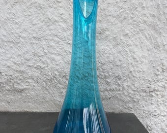 Pode incluir: Um vaso de vidro azul alto e fino com uma abertura alargada. O vaso tem um degradê de cor, começando com um azul mais claro na parte superior e passando para um azul mais escuro na parte inferior.