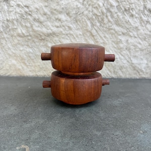 以下が含まれることがあります： 2つの木製ソルト＆ペッパーシェーカー。シェーカーは濃い茶色の木材でできており、両側に小さな水平ハンドルが付いた円筒形をしています。シェーカーは互いの上に積み重ねられています。