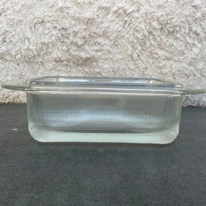 Puede incluir: Un plato rectangular de vidrio transparente con un diseño acanalado y bordes redondeados. El plato tiene dos pequeñas asas a los lados.