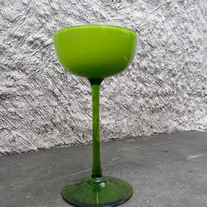 May include: A tall, green glass goblet with a wide, shallow bowl and a long, slender stem. The goblet is made of clear glass and has a green tint.