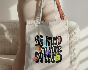 Könnte beinhalten: Beige Tragetasche mit dem Schriftzug "BE KIND TO YOUR MIND" in schwarzer Retro-Schrift. Das Design beinhaltet bunte florale Akzente in Orange, Blau, Rosa und Grün. Die Tasche hat lange Henkel und ist aus einem robusten Stoff gefertigt.