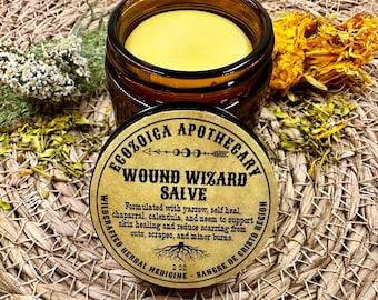 May include: An amber glass jar containing yellow salve, with a round label reading Ecozoica Apothecary Wound Wizard Salve, formulated with yarrow, self heal, chaparral, calendula, and neem, 2 oz. The lid is placed in front of the open jar.