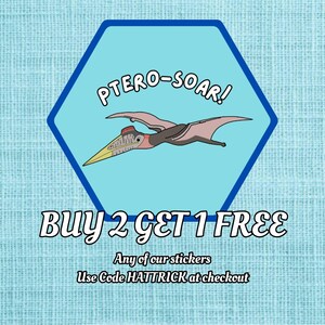 May include: A sticker featuring a cartoon pterodactyl with the text "PTERO-SOAR!" inside a blue hexagon. The sticker also includes the text "BUY 2 GET 1 FREE" and "Use Code HATTRICK at checkout."