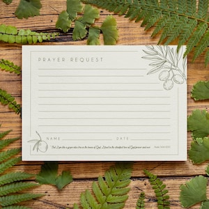 Puede incluir: Una tarjeta de solicitud de oración de color crema con espacios con líneas para escribir. La tarjeta presenta el texto "PRAYER REQUEST" en la parte superior y espacios para "NAME" y "DATE" en la parte inferior. Ilustraciones de ramas de olivo adornan la tarjeta, junto con un versículo bíblico.