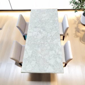 Puede incluir: Vista aérea de una mesa de comedor rectangular con una superficie texturizada gris claro. Cuatro sillas tapizadas beige con patas oscuras están dispuestas alrededor de la mesa. El texto "EpoxyDesignKING" es visible en la superficie de la mesa.