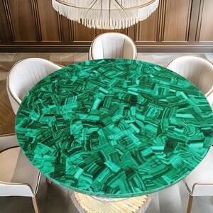 May include: A circular dining table featuring a striking green malachite surface. The table is encircled by four white chairs with gold detailing. The room has a warm ambiance, with wooden panelling and a chandelier.