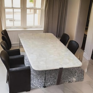 May include: A modern dining table with a white marble-like surface and dark metal legs. The table is surrounded by black leather chairs. The table is approximately 72 inches long and 40 inches wide, with a patterned base.