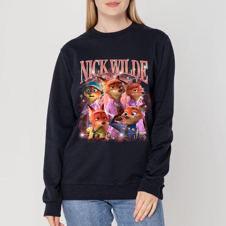 K&ouml;nnte beinhalten: Marineblaues Sweatshirt mit einem Aufdruck der Figur Nick Wilde aus dem Animationsfilm Zootopia. Das Bild enth&auml;lt den Text "NICK WILDE" in einer Retro-Schriftart, mit mehreren Cartoon-Fuchs-Charakteren. Das Sweatshirt hat lange &Auml;rmel.