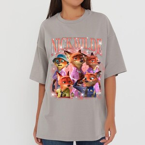 K&ouml;nnte beinhalten: Graues T-Shirt mit einem Aufdruck der Figur Nick Wilde aus dem Animationsfilm Zootopia. Der Aufdruck zeigt den Text "Nick Wilde" in einem Retro-Stil und Bilder von Nick Wilde in verschiedenen Outfits.