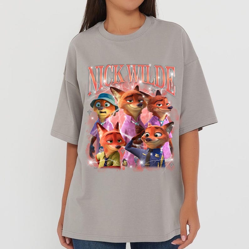 K&ouml;nnte beinhalten: Graues T-Shirt mit einem Aufdruck der Figur Nick Wilde aus dem Animationsfilm Zootopia. Der Aufdruck zeigt den Text "Nick Wilde" in einem Retro-Stil und Bilder von Nick Wilde in verschiedenen Outfits.