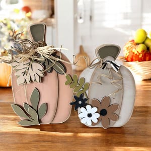 Pode incluir: Duas ab&oacute;boras de madeira decoradas para o outono. Uma &eacute; pintada de rosa com folhas verdes e a outra &eacute; pintada de branco com flores marrons e brancas.