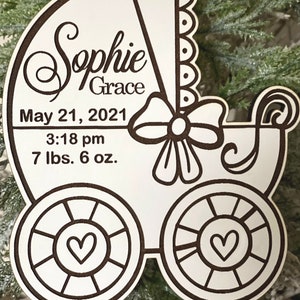 May include: White wooden baby carriage ornament with a black outline. The ornament is personalized with the name "Sophie Grace", the date "May 21, 2021", the time "3:18 pm", and the weight "7 lbs. 6 oz."