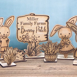 May include: Wooden cutout figures of bunnies, a sign that reads "Miller Family Farms Bunny Patch", and a basket of carrots. The figures are painted in brown and black, and the sign is painted in brown.