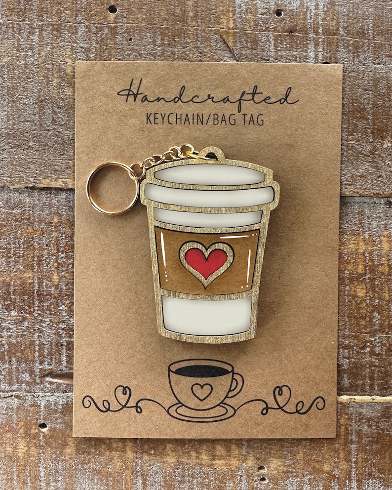 May include: Handcrafted wooden keychain or bag tag shaped like a coffee cup with a red heart on the side. The tag is on a brown card with the text "Handcrafted Keychain/Bag Tag".