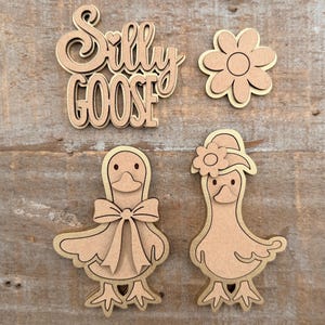 May include: Wooden cutouts of a flower, two geese, and the words "Silly Goose". The geese have bowties and hats. The cutouts are made of light brown wood with a darker brown outline.