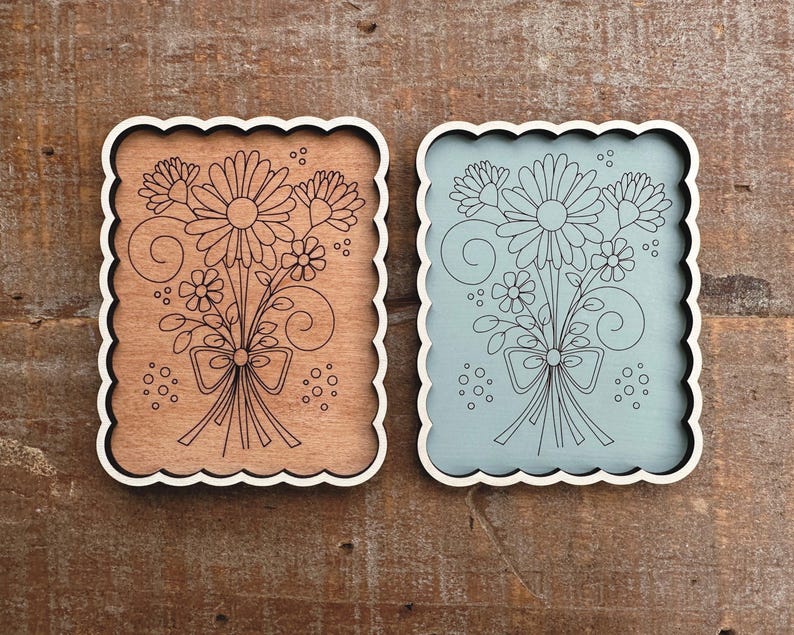 May include: Two decorative wooden plaques with scalloped edges. One is brown with a floral design, the other is light blue. Both feature a black line drawing of a flower bouquet tied with a bow. The plaques are rectangular with rounded corners.