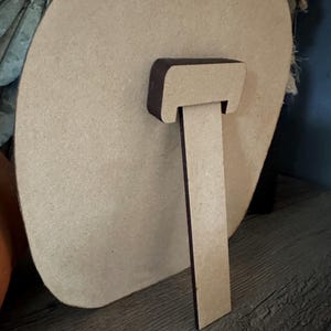 Pode incluir: Um sinal redondo de madeira inacabado com um cavalete de madeira marrom. O sinal est&aacute; em branco e pronto para ser pintado ou decorado.