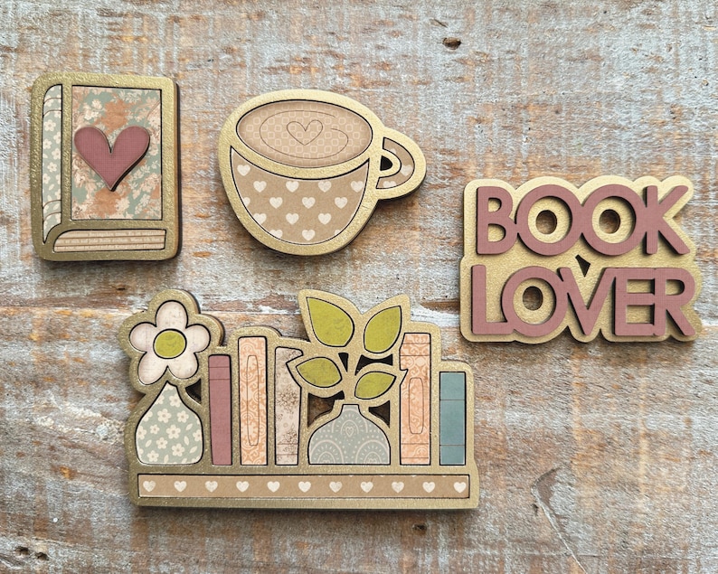 May include: Wooden decorative cutouts featuring a book, coffee cup, the words "BOOK LOVER", and a bookshelf with books and plants. The cutouts have gold edges and pastel colors, with heart and floral patterns.