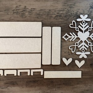 Puede incluir: Un conjunto de piezas de artesan&iacute;a de madera para crear un adorno de copo de nieve. El conjunto incluye una forma de copo de nieve, un coraz&oacute;n y varias piezas rectangulares.